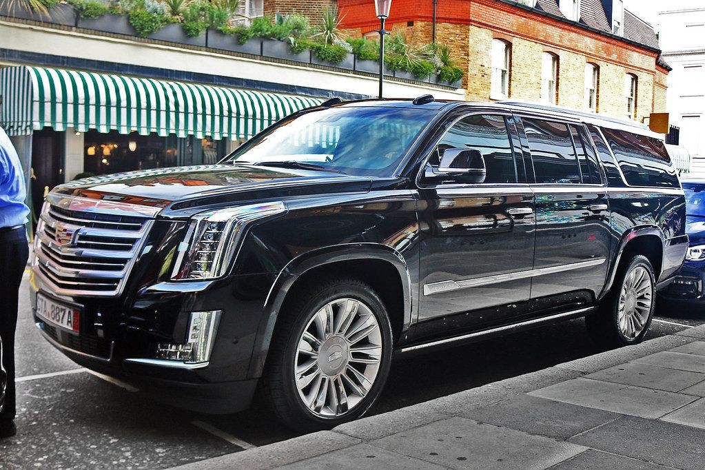 Black luxury SUV parked on a city street with striped awnings and brick buildings in the background.